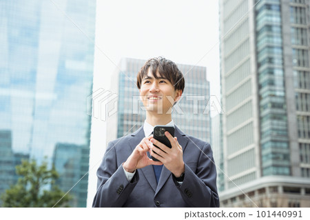一個 20 多歲和 30 多歲穿著西裝的男人在城市戶外用雙手操作智能手機時望著遠方 101440991