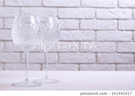 Two empty wine glasses on a table against a brick wall 101441017