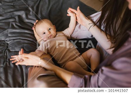 Cute baby is lying on the legs of a mother who is sitting on the bed 101441507