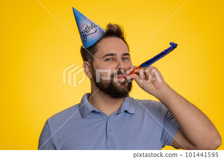 Happy excited lucky man wearing birthday hat cone blow pipe celebrating party success win victory 101441595