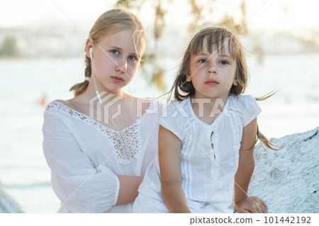 Two sisters, kid and teenage girl sitting on the tree against background of sea 101442192