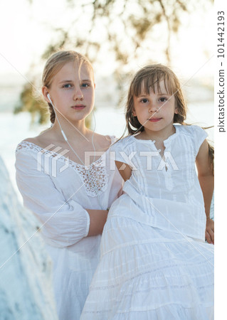Two sisters, kid and teenage girl sitting on the tree on the background of sea and sunlight 101442193
