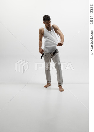 Portrait of attractive muscular man wearing classic pants and t-shirt touching clothes over white studio background. Attractive Portrait of attractive muscular man wearing classic pants and t-shirt touching clothes over white studio background. Attractive 101443528