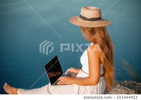 Freelance women sea working on the computer. Good looking middle aged woman typing on a laptop keyboard outdoors with a beautiful sea view. The concept of remote work. 101444452