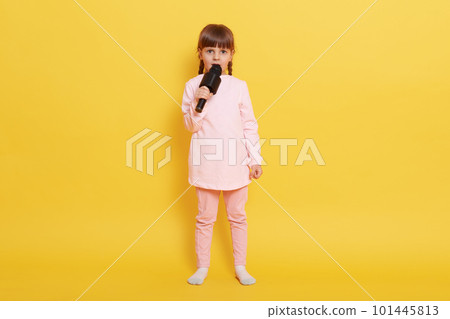 Charming little star singer with mic in hands sin gin g songs isolated over yellow background, looks at camera, full length photo of small cute vocalist arranging concert. 101445813
