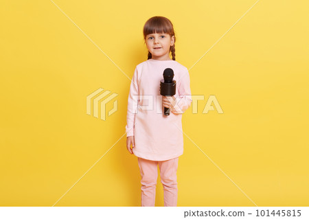Littler attractive girl wearing pale pink casual clothing standing isolated over yellow background, full length photo of charming vocalist performing at concert, looks at camera with excited look. 101445815