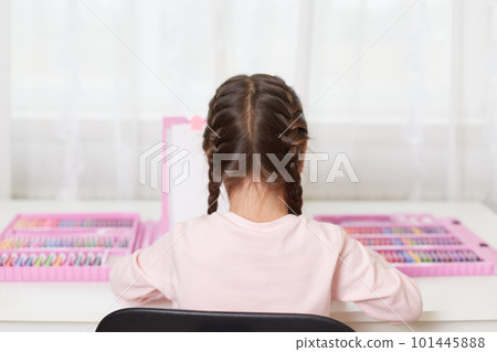 Back view of little girl with pigtails sitting at table in room and painting, child in casual clothing using drawing set, paints picture with crayons. Back view of little girl with pigtails sitting at table in room and painting, child in casual clothing using drawing set, paints picture with crayons. 101445888