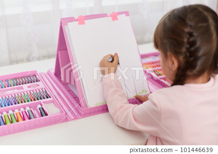 Child girl draws with colored pencils, diligent female kid using ruler for drawing straight line, sitting backwards to camera at desk with set of creativity. 101446639