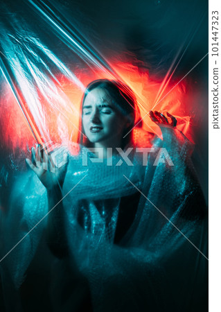 Plastic pollution. Global warming. Ecology problem. Red blue color light defocused woman suffocating in bubble wrap trapped in wrinkled polyethylene film. 101447323