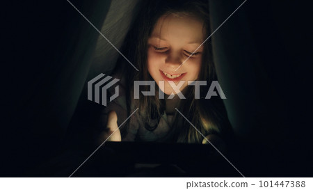 Bedtime movie. Night gadget. Restless kid. Amused little girl enjoying watching video cartoons on tablet under blanket late in dark. Bedtime movie. Night gadget. Restless kid. Amused little girl enjoying watching video cartoons on tablet under blanket late in dark. 101447388