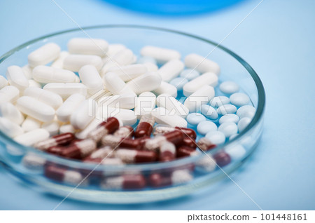 Selective focus on medical pills and gel translucent capsules with granules inside it scattered in petri dish over isolated blue background. World Health Day. Pharmaceutical business and industry 101448161