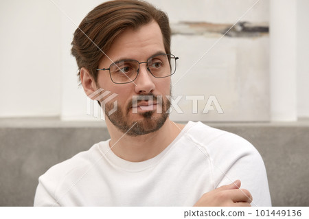 Close-up of a cheerful satisfied attractive man with stubble, with a wide smile, in round glasses, rejoices at success at work, stands against the backdrop of a cozy interior. Fashion designer happy 101449136