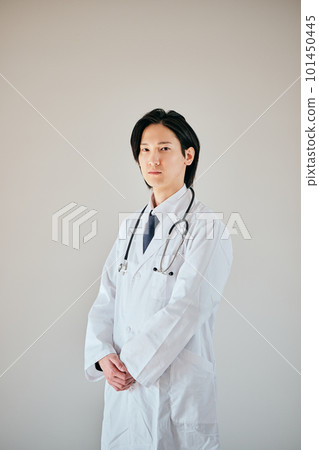 A young man in a white coat standing with his hands folded in front 101450445