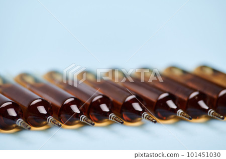 Background with a row of dark glass ampoules isolated on blue background. Healthcare and medicine concept. Injectable dosage forms. Selective focus. Copy advertising space. World Health Day Background with a row of dark glass ampoules isolated on blue background. Healthcare and medicine concept. Injectable dosage forms. Selective focus. Copy advertising space. World Health Day 101451030