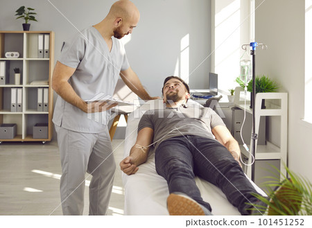 Man lying at doctor's office in clinic while receiving IV drip infusion and vitamin therapy. 101451252