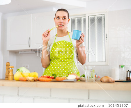 Housewife eating vegetable while cooking dinner at home 101451507
