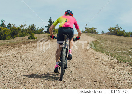 rear view athlete cyclist riding mountain bike uphill, biking on gravel road, cycling competition rear view athlete cyclist riding mountain bike uphill, biking on gravel road, cycling competition 101451774