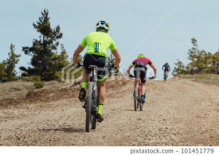 rear view group athlete cyclist riding mountain bike uphill, biking on gravel road, cycling competition rear view group athlete cyclist riding mountain bike uphill, biking on gravel road, cycling competition 101451779