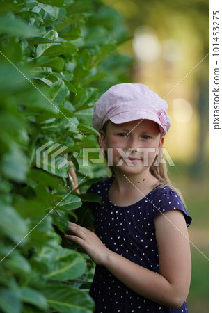 Cute caucasian little girl in a pink hat standing near the blooming bush of blue hydrangea. Selective focus Cute caucasian little girl in a pink hat standing near the blooming bush of blue hydrangea. Selective focus 101453275