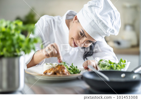 A young female chef finishes the meal with herbs in the restaurant kitchen A young female chef finishes the meal with herbs in the restaurant kitchen 101453308