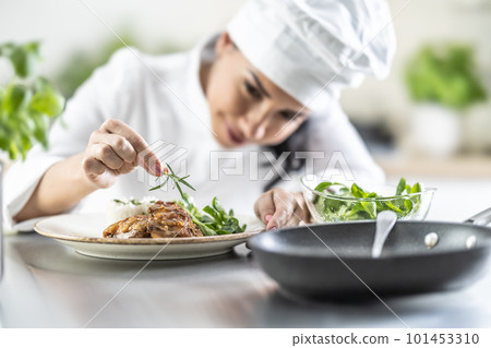 A young female chef finishes a meal with a sprig of rosemary in a restaurant kitchen 101453310