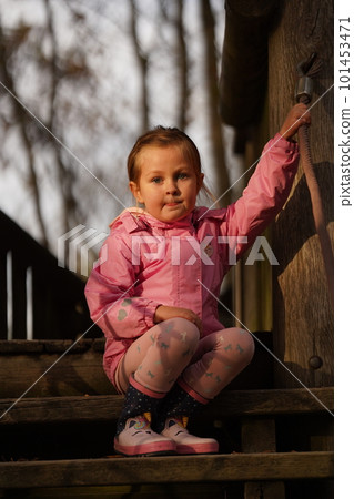 Cute girl in pink sits on wooden steps 101453471