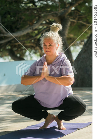 Serious aged woman in with dreadlocks hairstyle standing on beach against sea while practicing pose or asana during sunny day 101453685