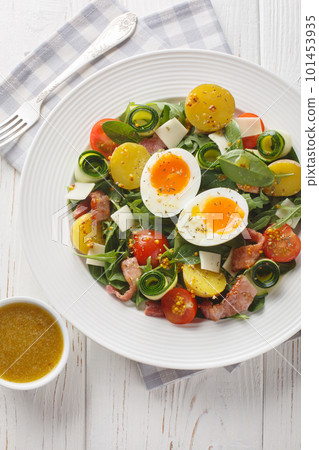 Peasant salad prepared with leafy vegetables, ham, cheese, tomatoes, potatoes and soft-boiled eggs closeup. Vertical top view 101453935
