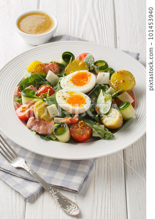 Fresh peasant salad with arugula, spinach, potatoes, bacon, tomatoes, cheese and soft-boiled eggs close-up on a plate. Vertical 101453940
