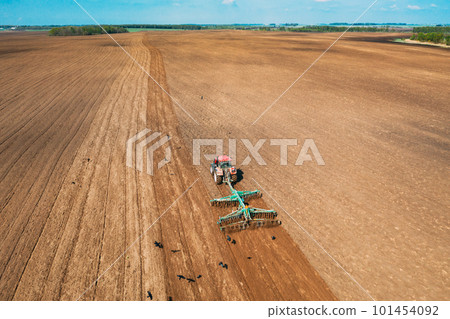 Aerial View. Tractor Plowing Field In Spring Season. Beginning Of Agricultural Spring Season. Cultivator Pulled By A Tractor In Countryside Rural Field Landscape Aerial View. Tractor Plowing Field In Spring Season. Beginning Of Agricultural Spring Season. Cultivator Pulled By A Tractor In Countryside Rural Field Landscape 101454092