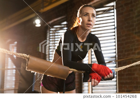 Woman fighter girl power. Woman fighter with red boxing wraps protective bandages standing on boxing ring leaning on ropes waiting resting. Strong powerful girl. Strength fit body workout training 101454268