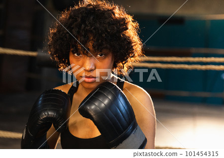 Outcry independent girl power. Angry african american woman fighter with boxing gloves looking serious aggressive standing on boxing ring. Strong powerful fighter girl training punches Outcry independent girl power. Angry african american woman fighter with boxing gloves looking serious aggressive standing on boxing ring. Strong powerful fighter girl training punches 101454315