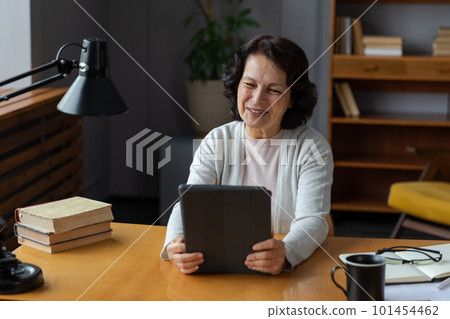 Happy middle aged senior woman holding tablet talk on video call with friends family. Laughing mature old senior grandmother having fun talking speaking with grown up children online Happy middle aged senior woman holding tablet talk on video call with friends family. Laughing mature old senior grandmother having fun talking speaking with grown up children online 101454462