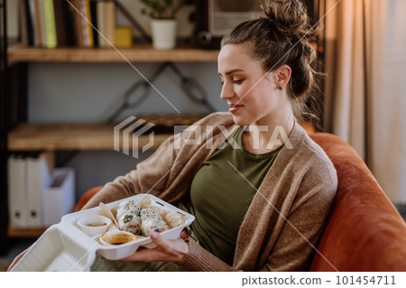 Young woman enjoying delivered food in her living room. Young woman enjoying delivered food in her living room. 101454711