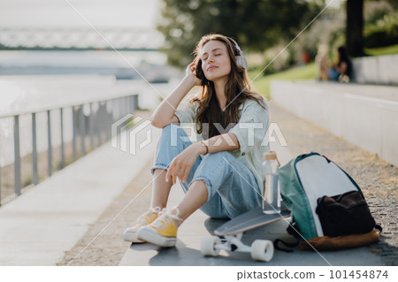 Happy young woman sitting in city and listening music. Youth culture and commuting concept. 101454874