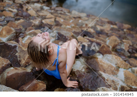 Rear view of happy young woman resting and sunbathing in swimsuit near lake, during hot sunny day on summer vacation. 101454945