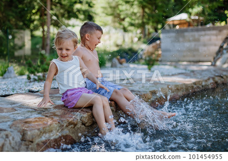 Cute girl and boy sitting together on the footpath by the lake, dangle their feet in the water, summer vacation concept. Cute girl and boy sitting together on the footpath by the lake, dangle their feet in the water, summer vacation concept. 101454955