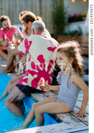 Multi generation family enjoying summer time, sitting at backyard pool. 101454973