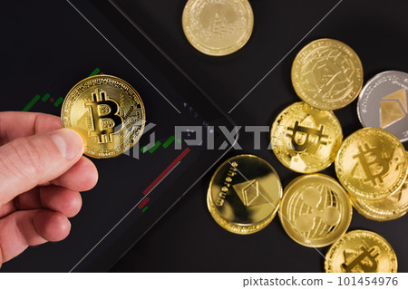 Hand holding Bitcoin over digital tablet by coins 101454976