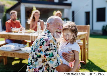 Happy little girl giving birthday present to her senior grandfather at generation family birthday party in summer garden 101454977