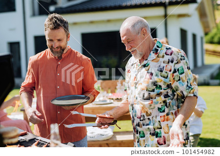 Senior father with adult son grilling outside on backyard in summer family during garden party 101454982