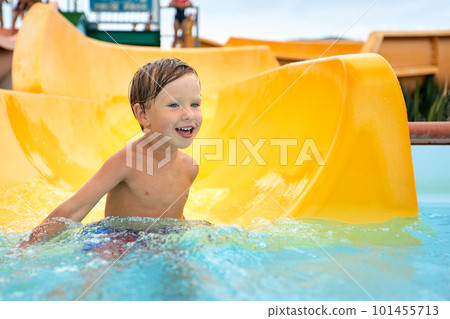 Cheerful blue-eyed kid on a water slide in the water park, a little boy merrily slides into the water along the slide in the amusement park, rest with children in the water park Cheerful blue-eyed kid on a water slide in the water park, a little boy merrily slides into the water along the slide in the amusement park, rest with children in the water park 101455713