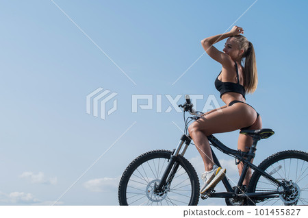 Caucasian woman with a stunning athletic figure in short shorts rides a bike against the blue sky 101455827