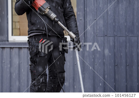 A worker installs a ground rod to ground a building. A worker in work clothes drives earth rods into the ground with a jackhammer to prevent short circuits. A worker installs a ground rod to ground a building. A worker in work clothes drives earth rods into the ground with a jackhammer to prevent short circuits. 101456127