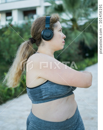 Young pretty body positivity plus size woman in sporty top and leggings doing sport fitness and listen to music with headphones in summer morning outdoor Young pretty body positivity plus size woman in sporty top and leggings doing sport fitness and listen to music with headphones in summer morning outdoor 101456191