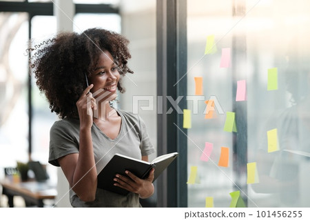 Young African American woman pin weekly planning sticker on the window at home. 101456255