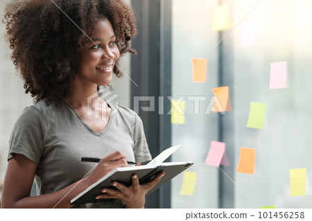 Young African American woman pin weekly planning sticker on the window at home. 101456258