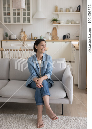 Cheerful attractive mature woman sitting on soft couch at home 101456721