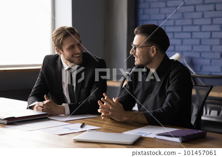 Two cheerful happy business partners men talking at work table Two cheerful happy business partners men talking at work table 101457061
