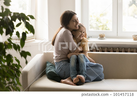 Joyful mom cuddling sweet little girl on home sofa 101457118